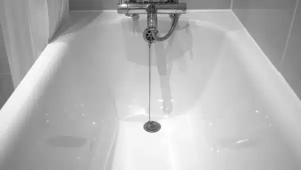 A white bathtub with a chrome faucet and attached chain leading to the drain, set against tiled walls.
