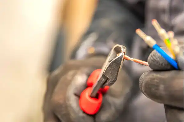 Gloved hand using red-handled wire cutters to strip insulation from electrical wires.