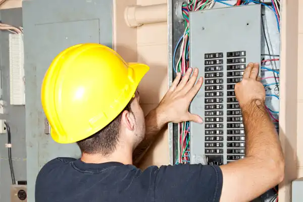 Person in a yellow hard hat working on an electrical panel with exposed wires.
