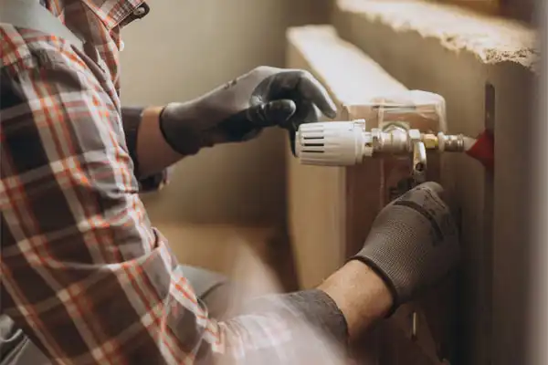 Person in plaid shirt and gloves adjusting a radiator valve.