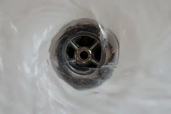 Close-up of water swirling down a metal drain, creating a vortex pattern.