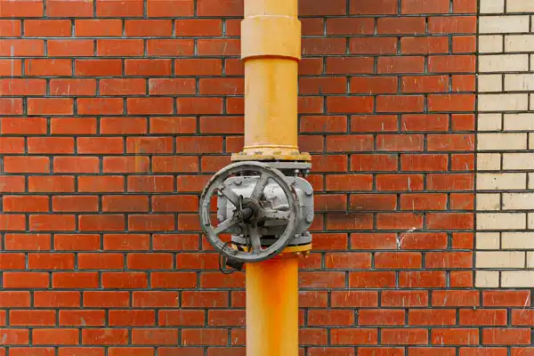 Orange pipe with a metal valve against a red and beige brick wall.
