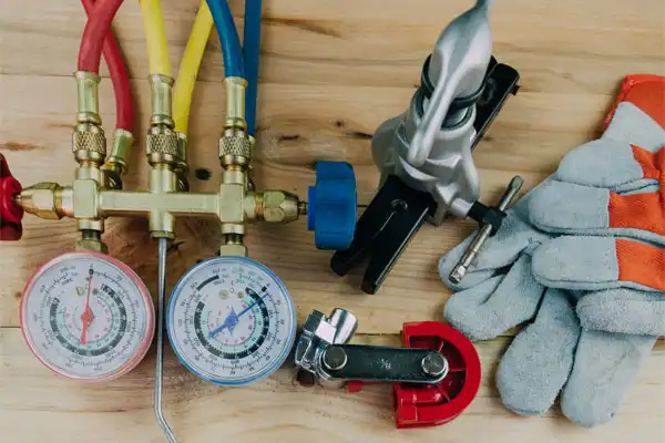 HVAC tools including gauges with hoses, gloves, and a tubing cutter arranged on a wooden surface.