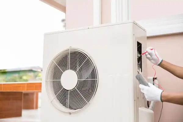 Person in gloves using a tool to service an air conditioning unit outdoors.