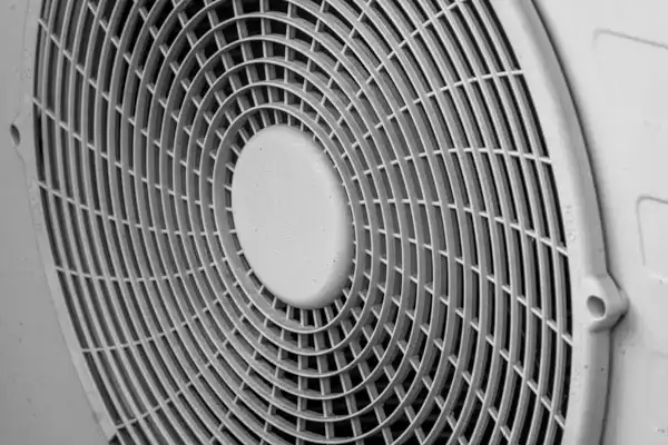 Close-up of a circular fan with a protective grid cover in a grayscale image.