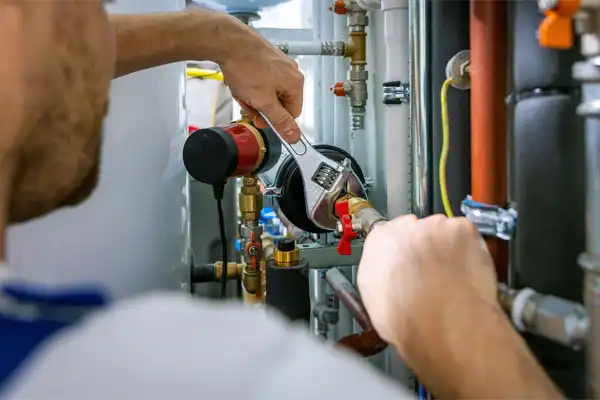 A person adjusts a pipe with a wrench amid various plumbing connections and valves.