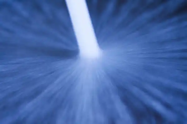 Blurry image showing a bright white streak amid dark blue radial blur, suggesting motion or speed.