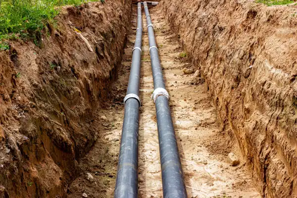 Two large black pipes laid in a trench surrounded by dirt, likely for utility installation or drainage.