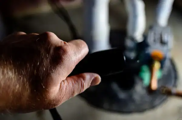 A hand holding a black object in the foreground, with blurred figures of two white statues and a paintbrush in the background.