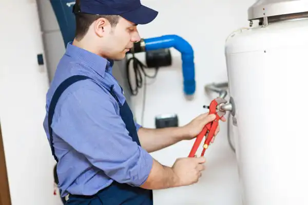 Worker in blue uniform and cap uses wrench on a water heater.