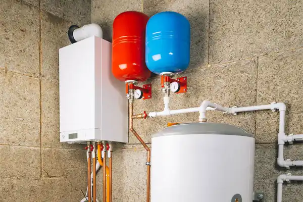 A boiler system with red and blue expansion tanks mounted on a wall, connected with pipes, in a utility room.