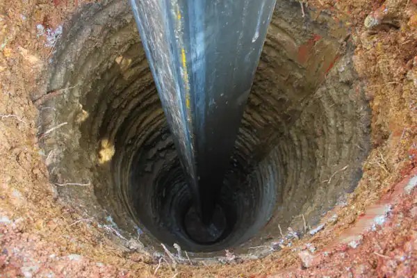A close-up view of a deep vertical well in the ground with a large black pipe inserted into it.