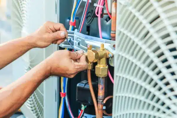 Person working on electrical wires and components inside an HVAC unit, using a wrench.