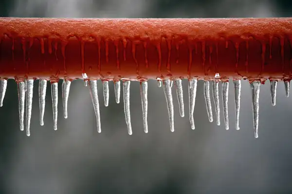 Icicles hanging from a red pipe against a gray background.